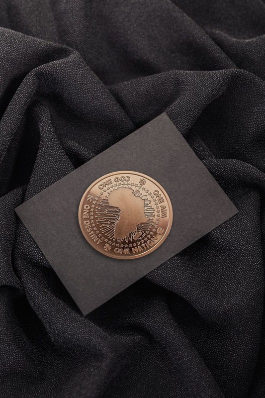 The copper Genesis Medallion resting on the black Legacy Card, on dark fabric
